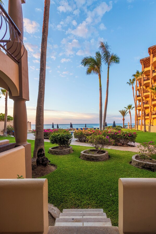 A resort courtyard with palm trees, a pool, and a view of the ocean.
