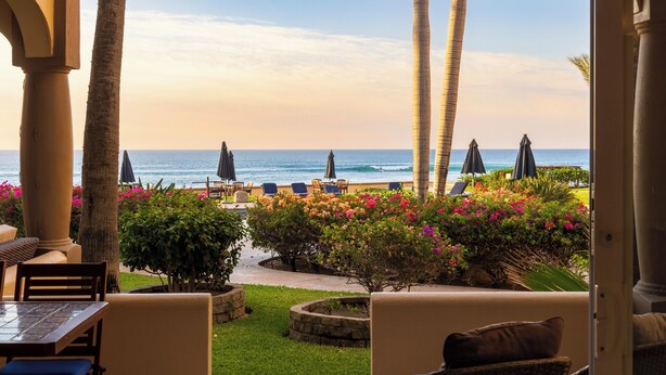 A patio with outdoor seating, palm trees, and a view of the ocean. - Surf & Stay; Beachfront Condo Steps from Sand - Heated Hot tub -Pool-Pickleball (San José del Cabo)