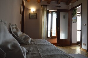 Un dormitorio con cama, mesita de noche, lámpara de pared, puerta con cristal esmerilado y vistas al exterior.