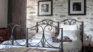 A bedroom with a metal bed frame, a brick-patterned wall, and framed pictures. - Sarkeep - Villa Immersed in the vineyards of Taurasi (Luogosano (Avellino))