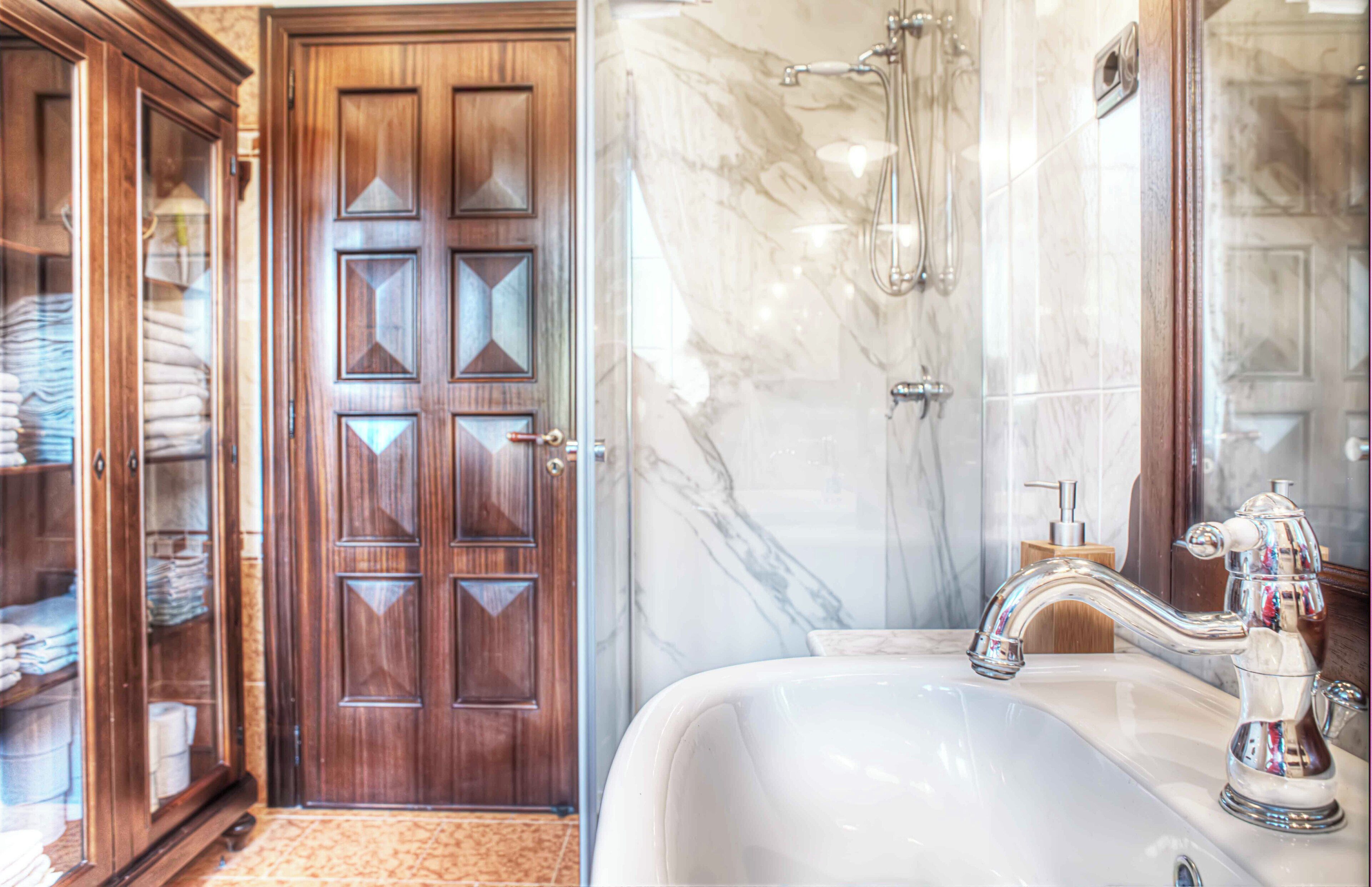 Une salle de bain avec un mur en marbre, une porte en bois et un lavabo blanc doté d’un robinet chromé.