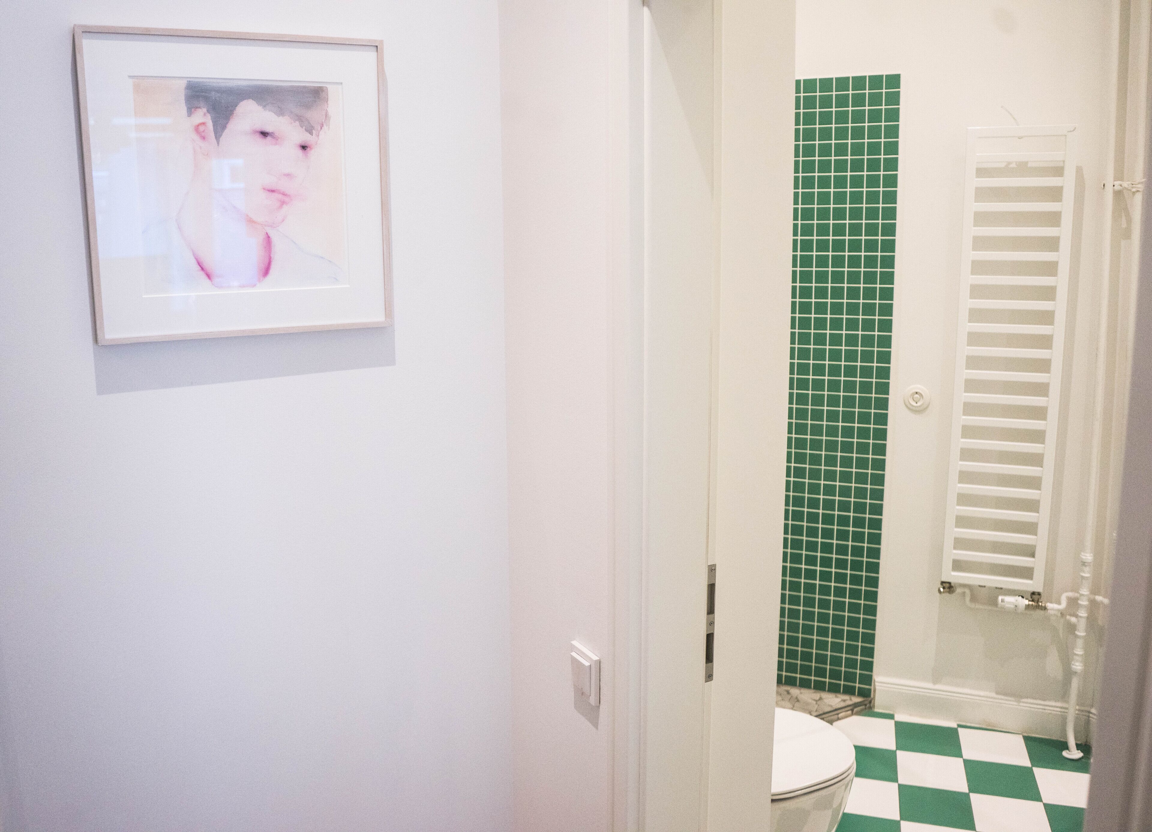 A bathroom with a green tiled shower wall, a white toilet, and a framed picture on the wall.