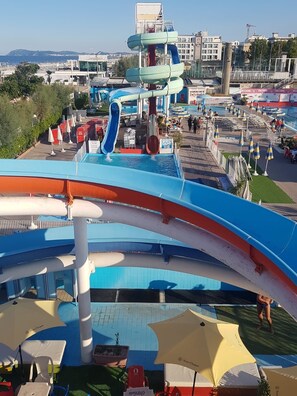 Een waterpark met glijbanen en zwembaden, omringd door parasols en ligbedden.