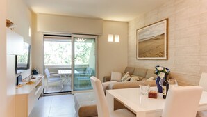 A modern living room with a sofa, a dining table, and a TV. There is a sliding glass door leading to an outdoor area with chairs. - RICCIONE with BEACH and AQUAPARK INCLUDED /BEACH and AQUAPARK included !!! (Riccione)