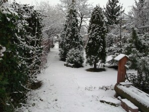 Sentiero innevato circondato da alberi sempreverdi e una costruzione in legno.