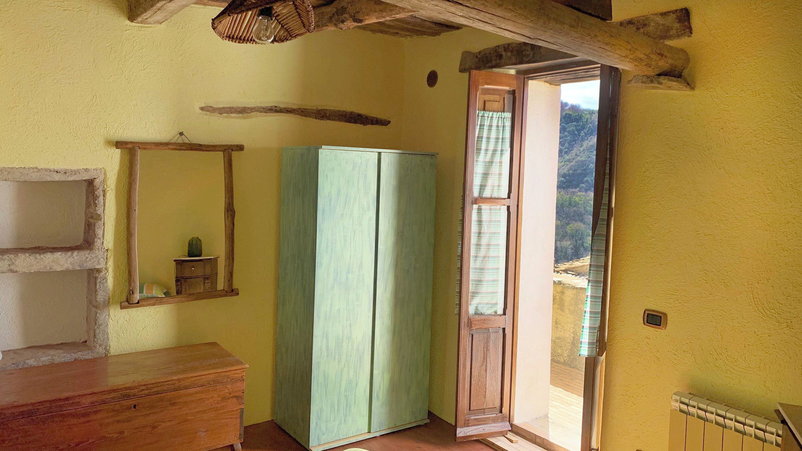 Une pièce comprenant une commode en bois, une armoire verte, un luminaire suspendu et une porte donnant sur un espace extérieur.