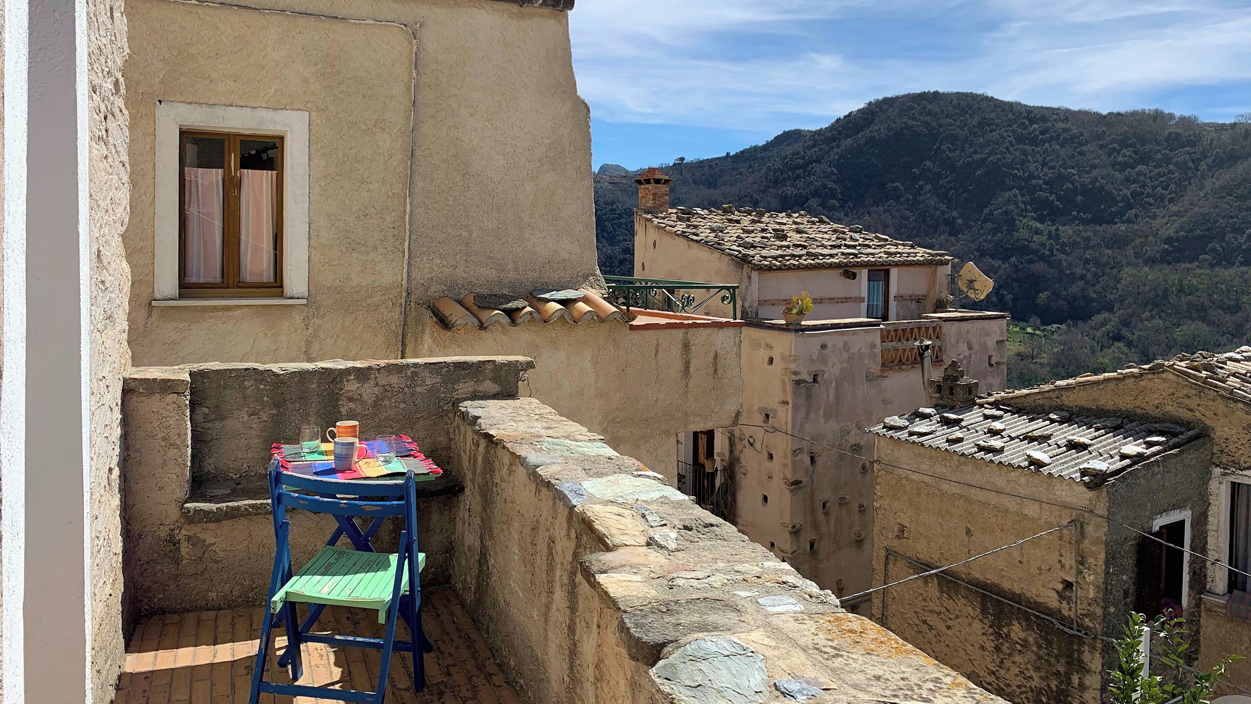 Un balcón rústico con mesa y sillas, con vistas a una colina.