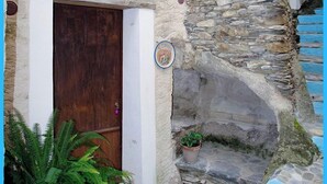 Un étroit escalier en pierre mène à une porte en bois, agrémentée de plantes en pot et d’une petite pancarte fixée au mur.