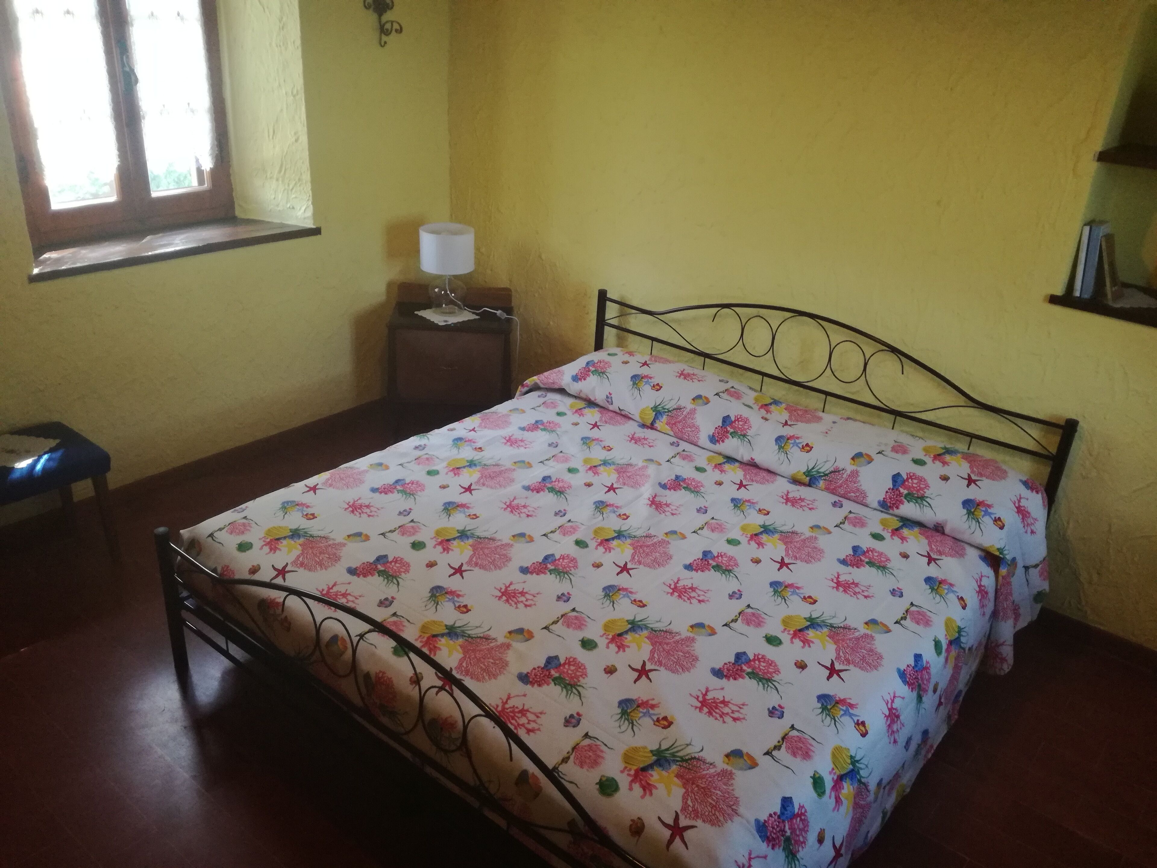Une chambre à coucher avec un lit, une table de chevet, une lampe, une fenêtre et une étagère.