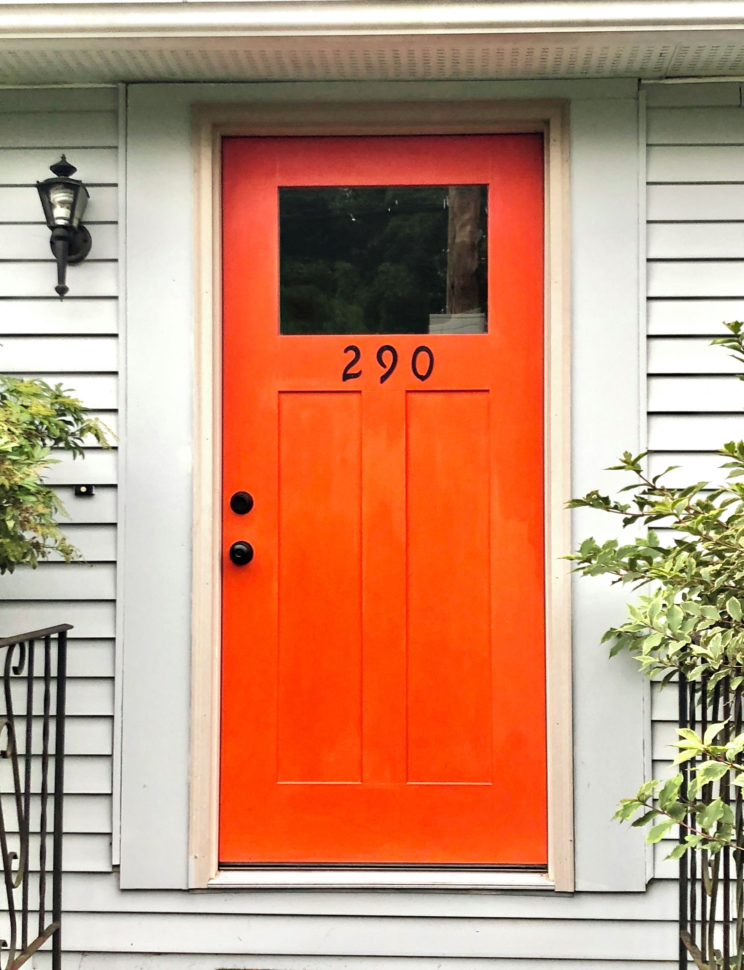 Eine leuchtend orangefarbene Tür mit der Nummer 290, ein kleines Fenster darüber und ein schwarzer Briefkasten zur Linken.