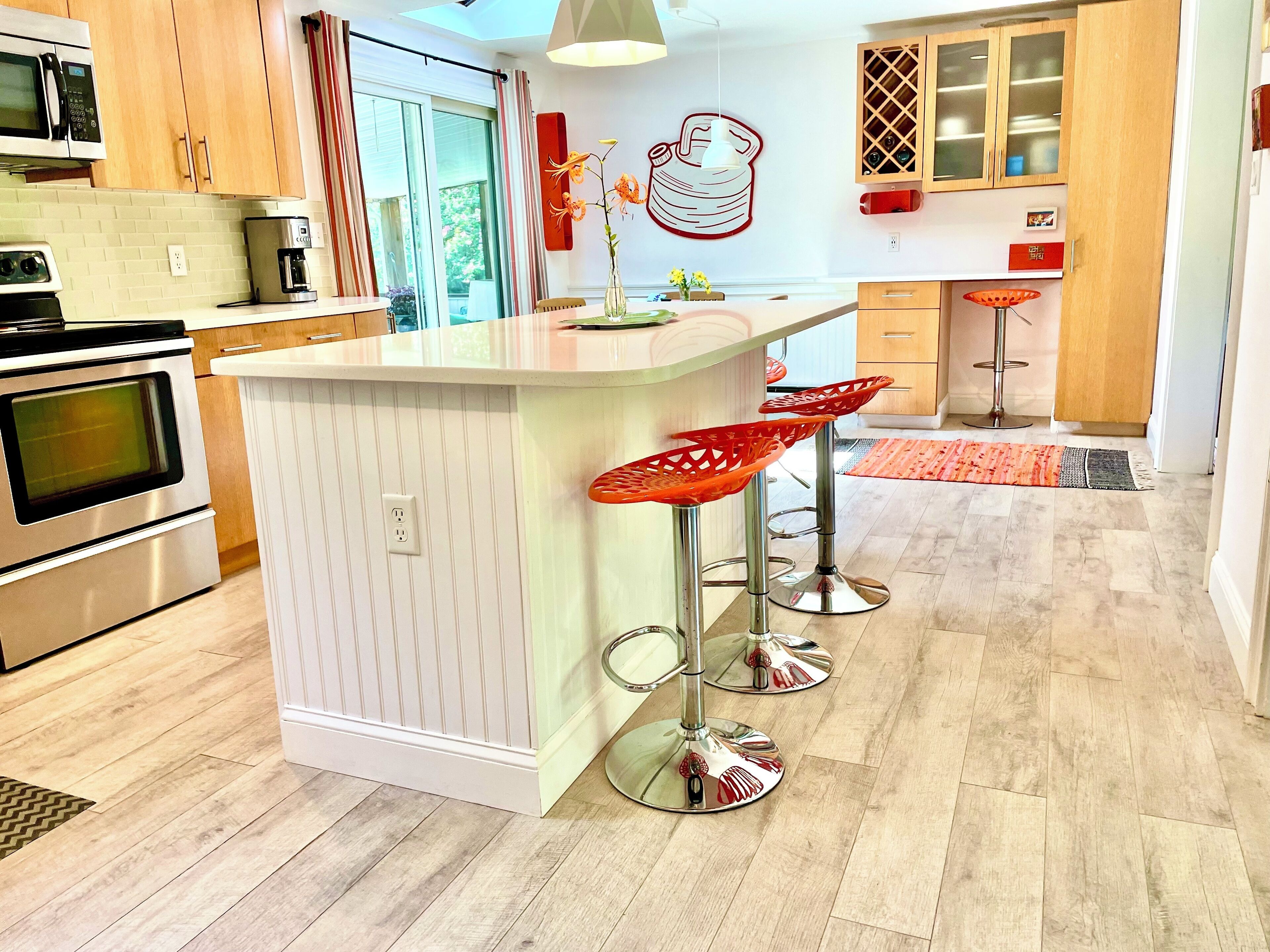 A modern kitchen with a central island, stainless steel appliances, and red bar stools.
