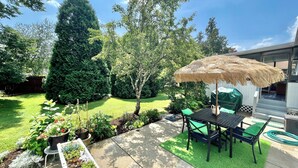 En terrasse med et bord og stole, en strålpavillon og en have med forskellige planter og græsplæne.