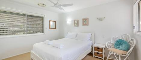 A bedroom with a bed, a ceiling fan, a window with blinds, a nightstand, a chair, and wall-mounted lights.