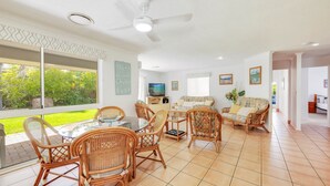 A spacious living area with a dining table, wicker chairs, a sofa, and a TV. - 22 Bussey Street Bargara (BARGARA)
