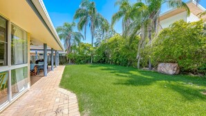 A modern house with a covered patio, a well-maintained lawn, and tall palm trees. - 22 Bussey Street Bargara (BARGARA)