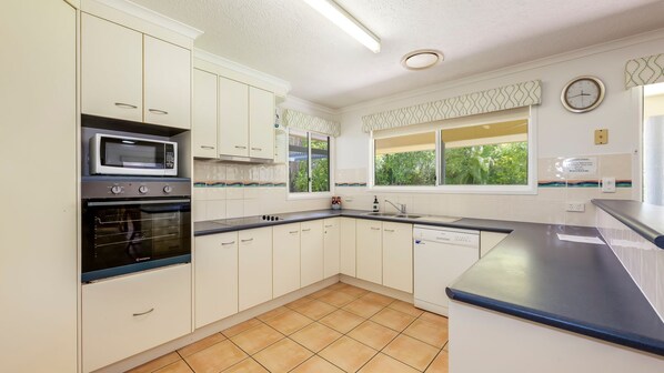 Una cocina con armarios blancos, microondas, horno, lavavajillas y una ventana con vistas al verdor.