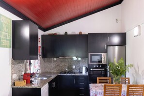 A compact kitchen with dark cabinets, a microwave, a refrigerator, a sink, and a dining table with chairs.