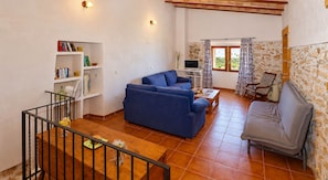 Uma sala de estar com um sofá azul, uma poltrona cinza, uma mesa de centro de madeira e uma estante de livros.
