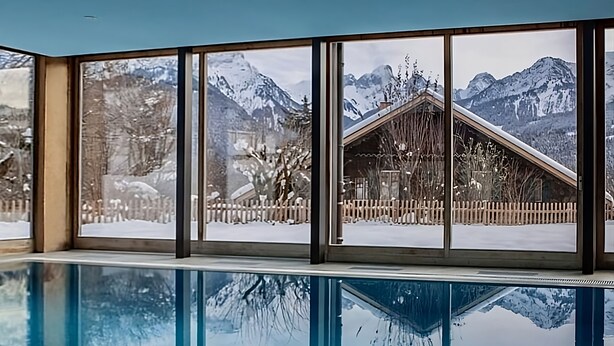 A pool with a view of snowy mountains and a wooden cabin. - Luxury 3 Bed apartment,  panoramic mountain views,  5* Spa Facilities - (La Soldanelle)