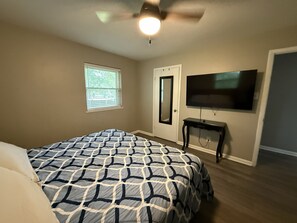 Une chambre à coucher avec un lit, un ventilateur de plafond, une télévision et une porte.