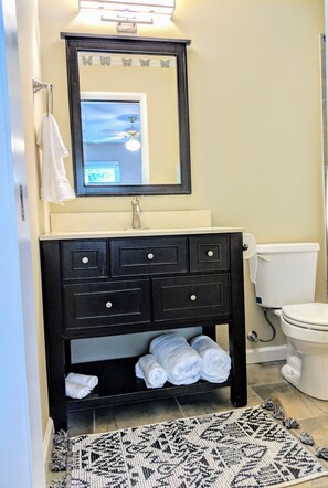 Een badkamer met een zwart badkamermeubel, een spiegel en een toilet. Handdoeken liggen op het meubelstuk en een kleed op de vloer.