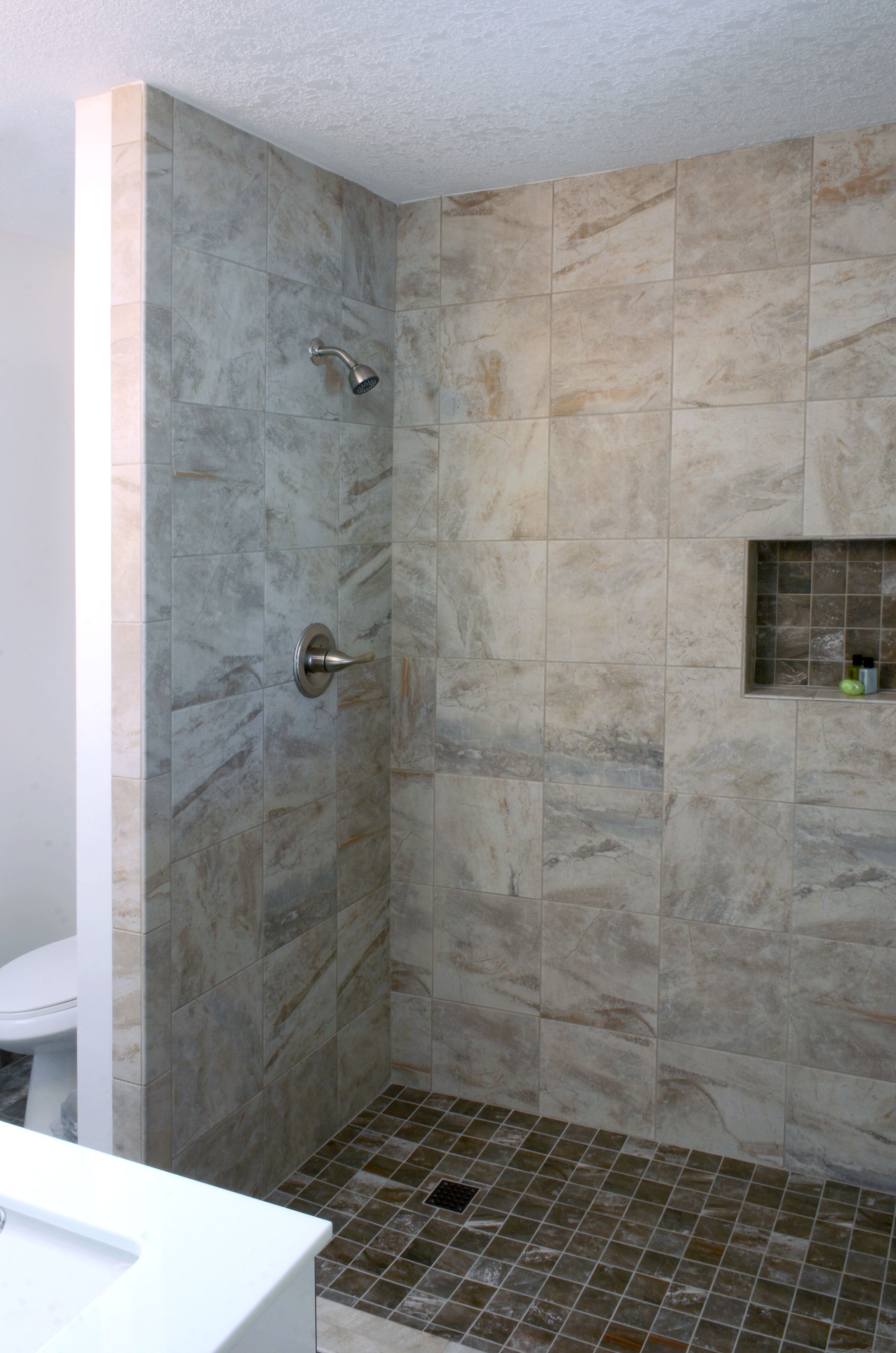 A bathroom with a shower, tiled walls, and a small shelf with toiletries.