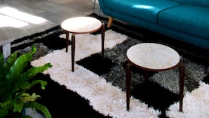 Ein Wohnzimmer mit einem türkisfarbenen Sofa, einem Couchtisch und einem kleinen runden Tisch. Eine Zimmerpflanze und ein Gemälde sind an der Wand zu sehen.