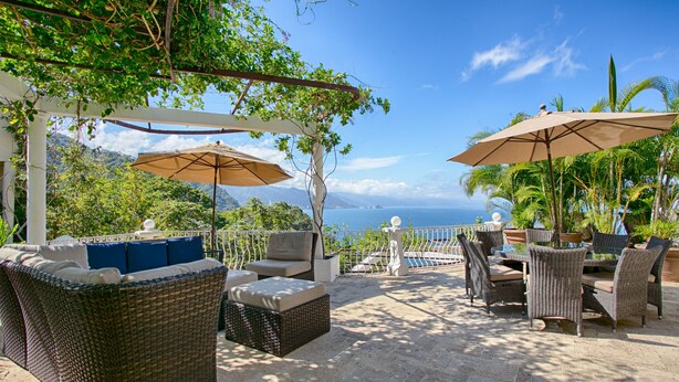 Un patio al aire libre con mobiliario de mimbre, sombrillas y vista al océano.