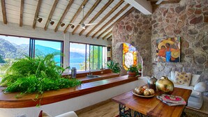 Amplia sala de estar con pared de piedra, vigas de madera, ventanas grandes y vista a las montañas.