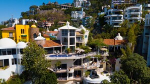 Un hotel de varios pisos con piscina, balcones y abundante vegetación.