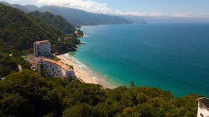 Un hotel frente al mar con vistas a la playa, rodeado de exuberante vegetación y montañas.