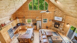 Ein gemütliches Blockhaus mit Kamin aus Stein, Holzwänden, einem Essbereich und einem großen Fenster mit Blick auf den Wald.