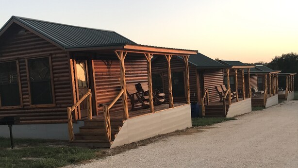 Uma fileira de cabanas de toras com varandas de madeira e degraus que levam à entrada.