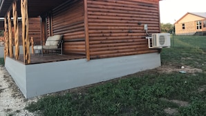 Uma cabana de registos com varanda, uma cadeira e um aparelho de ar condicionado.