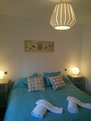 Un dormitorio con cama, almohadas, una obra de arte en la pared y lámparas de noche.