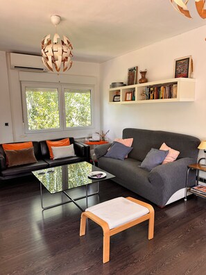 A modern living room with a sofa, a glass coffee table, a bench, and a bookshelf.