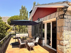 A patio with outdoor furniture, a large umbrella, and a stone building with a red awning.
