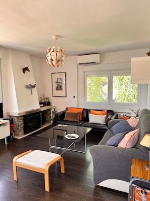 A modern living room with a stone fireplace, a black leather sofa, a glass coffee table, and a wooden bench.