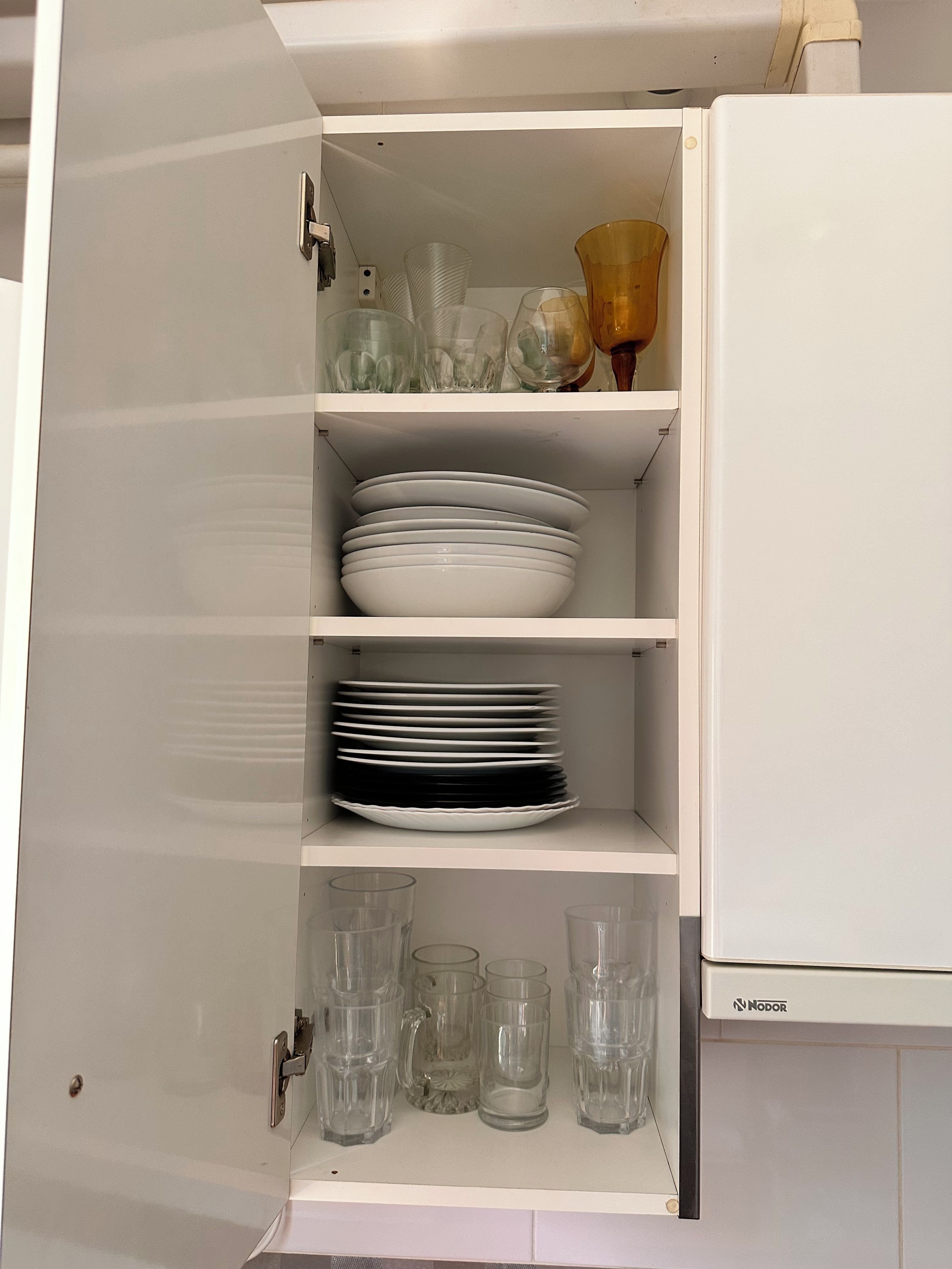 A kitchen cabinet with shelves containing plates, glasses, and a coffee pot.