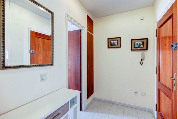Un couloir avec un mur blanc, une porte en bois, un miroir et deux tableaux encadrés.