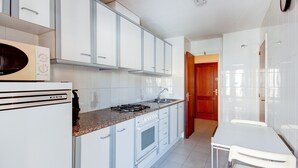 A kitchen with white cabinets, a stove, a sink, and a dining area with a table and chairs. - FRANCESC MACIA 57 3B  Roses (Rosas / Roses)