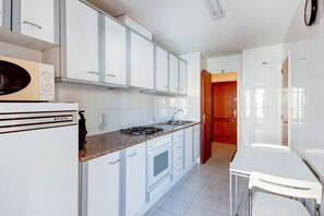 A kitchen with white cabinets, a stove, a sink, and a dining area with a table and chairs.