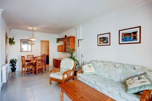 Ein Wohnzimmer mit einer Couch, einem Holztisch, einem Esstisch mit Stühlen und einer Küchenzeile mit Schränken und einer Pflanze.