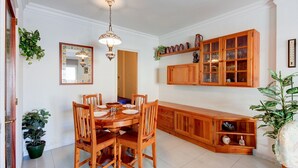 A dining area with a wooden table and chairs, a hanging light fixture, and a wooden cabinet with glass doors. - FRANCESC MACIA 57 3B  Roses (Rosas / Roses)