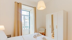 Een hotelkamer met een bed, een stoel, een garderobe en een deur die leidt naar een balkon.