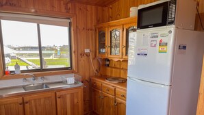 Une cuisine avec des meubles en bois, un réfrigérateur blanc, un four à micro-ondes et une fenêtre donnant sur un paysage verdoyant.