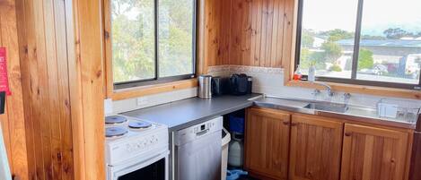 A compact kitchen with wooden walls, a stove, a dishwasher, and a sink.