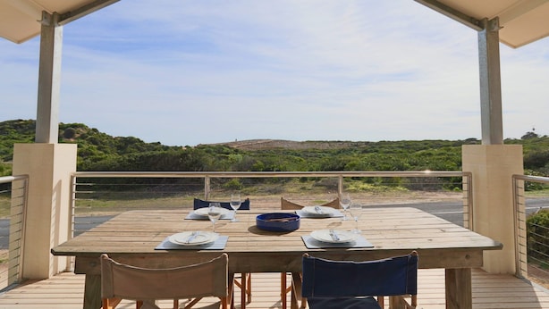 A wooden table set for two with plates, cutlery, and glasses, under a covered patio with a view of a hilly landscape. - Love Shack - Location and views this property has it all (Robe)