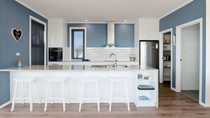 A modern kitchen with a central island, bar stools, a built-in oven, and a microwave. - Love Shack - Location and views this property has it all (Robe)