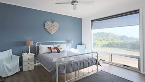 A bedroom with a bed, bedside tables, a chair, a heart-shaped wall decoration, and a large window with a view of greenery. - Love Shack - Location and views this property has it all (Robe)